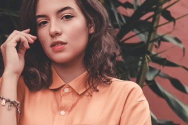 A girl wearing an orange shirt with a plant in the background