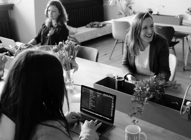 Three women working on laptops in an office, one of them smiling